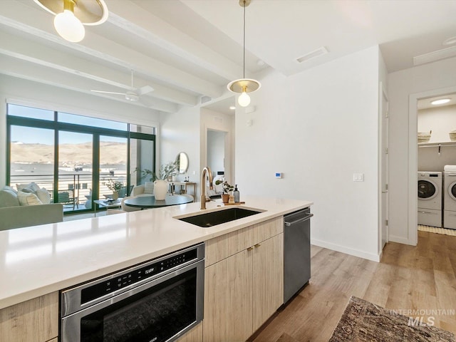 kitchen with dishwasher, pendant lighting, sink, light brown cabinets, and separate washer and dryer