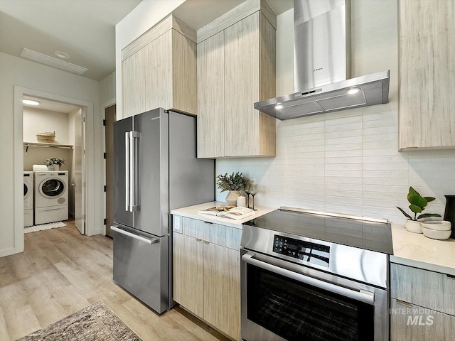 kitchen featuring independent washer and dryer, appliances with stainless steel finishes, wall chimney range hood, and light brown cabinets