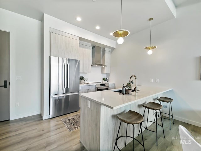 kitchen with appliances with stainless steel finishes, wall chimney exhaust hood, pendant lighting, a breakfast bar, and sink