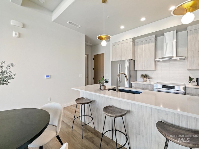 kitchen featuring tasteful backsplash, hanging light fixtures, appliances with stainless steel finishes, a breakfast bar area, and wall chimney exhaust hood