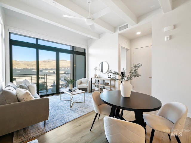 dining space with light wood-type flooring, ceiling fan, a wealth of natural light, and beamed ceiling