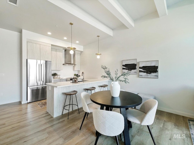 dining space with beam ceiling, sink, and light hardwood / wood-style floors