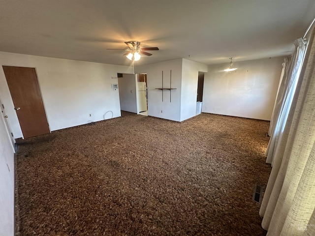 unfurnished bedroom featuring dark colored carpet, white fridge, and ceiling fan