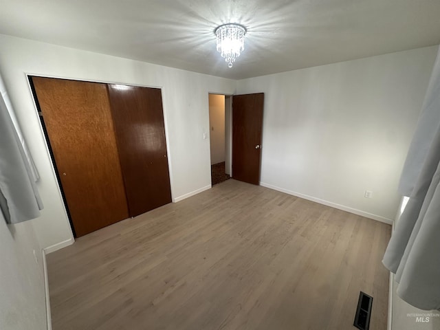 unfurnished bedroom featuring light hardwood / wood-style floors, an inviting chandelier, and a closet