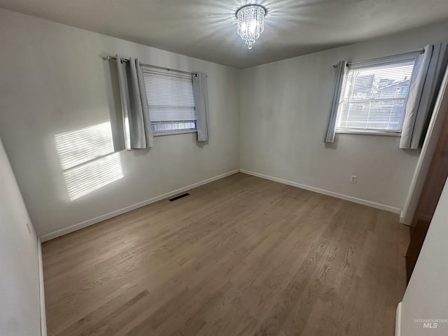 spare room with a chandelier and wood-type flooring