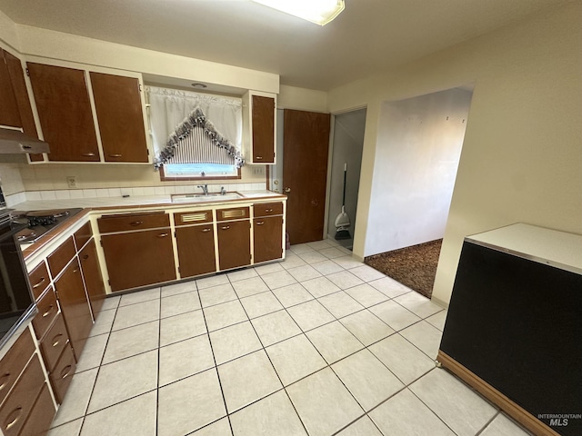 kitchen with light tile patterned floors, dark brown cabinetry, black gas stovetop, and sink