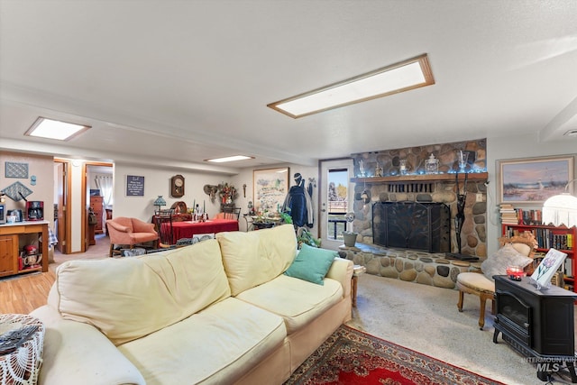 living area with a wood stove, a stone fireplace, and wood finished floors