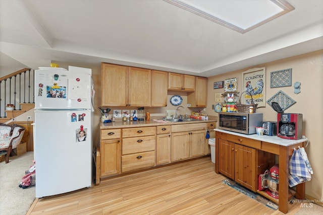 kitchen featuring freestanding refrigerator, light countertops, stainless steel microwave, a sink, and light wood finished floors