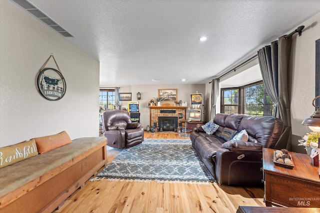 living room featuring a brick fireplace, a textured ceiling, plenty of natural light, and wood finished floors