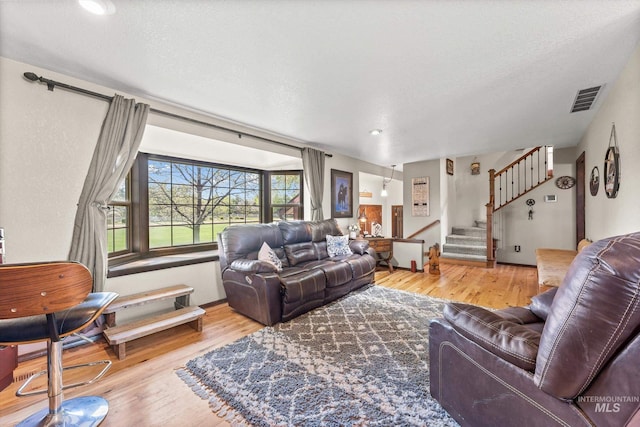 living area featuring stairs, a textured ceiling, visible vents, and wood finished floors