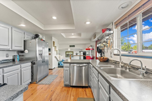 kitchen featuring appliances with stainless steel finishes, a sink, a peninsula, light wood-style floors, and a tray ceiling