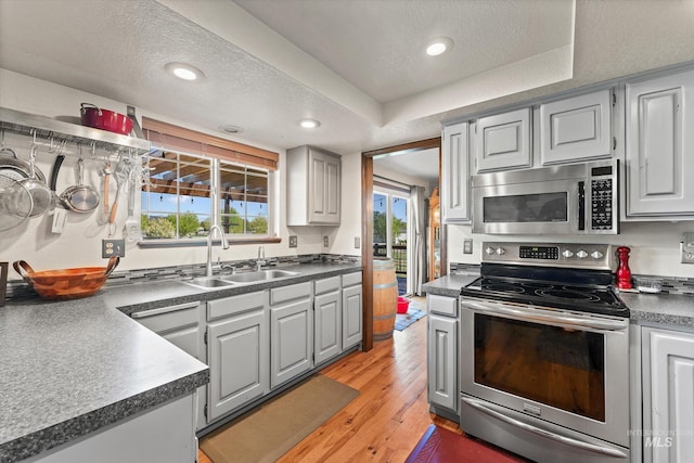 kitchen with dark countertops, a sink, light wood finished floors, stainless steel appliances, and recessed lighting