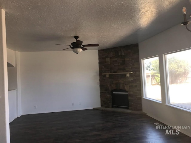 unfurnished living room with a stone fireplace, ceiling fan, dark hardwood / wood-style flooring, and a textured ceiling