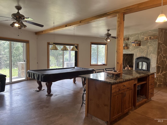 playroom featuring pool table, a stone fireplace, ceiling fan, beam ceiling, and concrete flooring