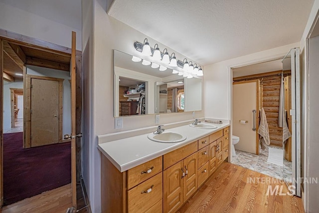 bathroom featuring double vanity, rustic walls, a sink, and toilet