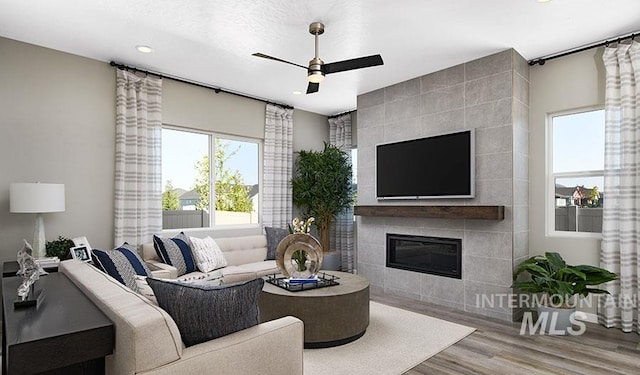 living room featuring a tiled fireplace, ceiling fan, and wood finished floors