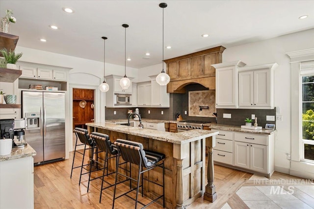 kitchen with white cabinetry, stainless steel appliances, a kitchen breakfast bar, a center island with sink, and decorative light fixtures