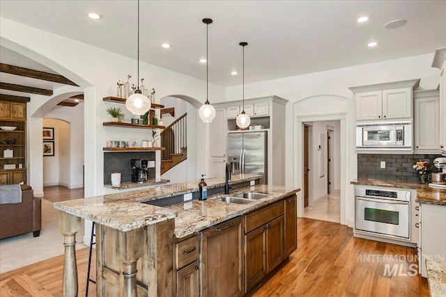 kitchen featuring pendant lighting, sink, stainless steel appliances, tasteful backsplash, and an island with sink