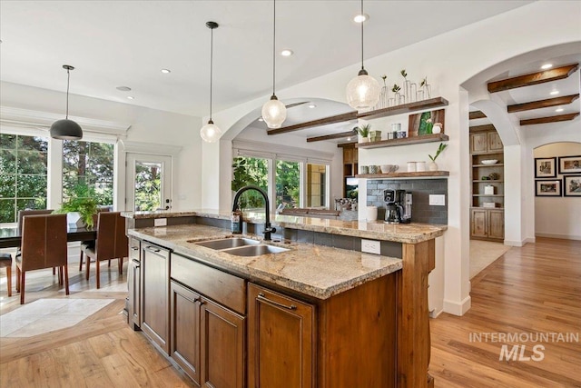 kitchen featuring light stone counters, hanging light fixtures, sink, and a center island with sink