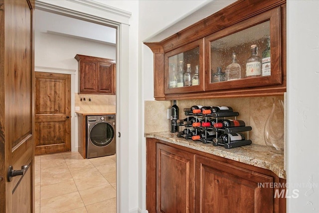 bar featuring light stone countertops, washer / dryer, light tile patterned floors, and decorative backsplash