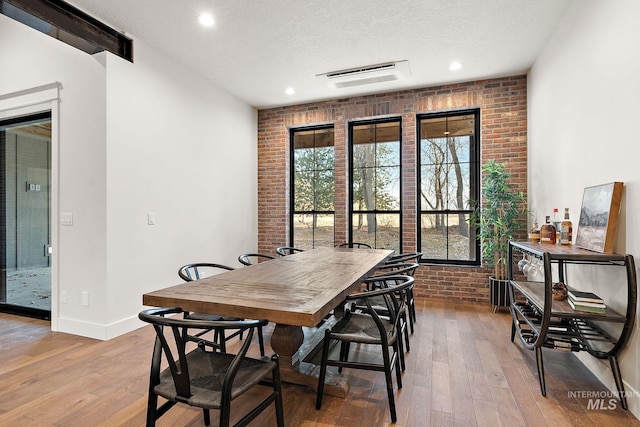 dining area with brick wall, light hardwood / wood-style floors, and a textured ceiling