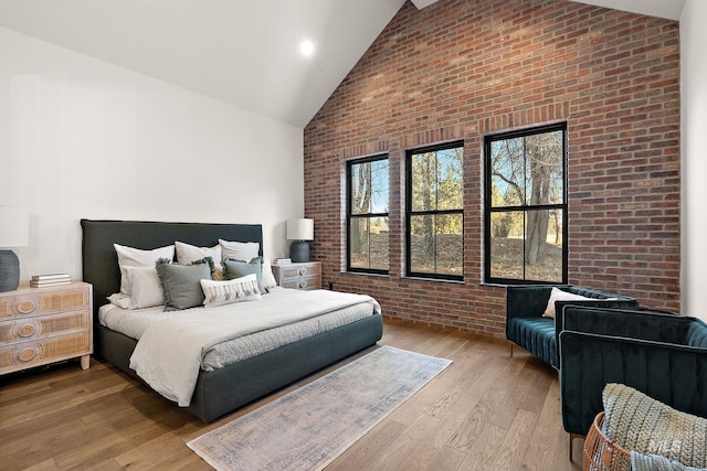 bedroom featuring wood-type flooring, high vaulted ceiling, and brick wall