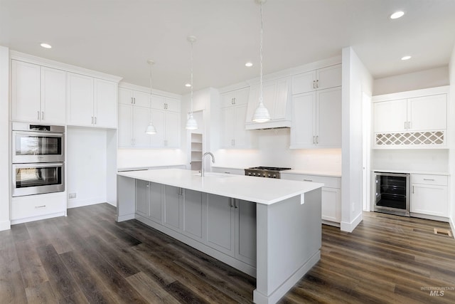 kitchen with beverage cooler, stainless steel double oven, a kitchen island with sink, a sink, and range