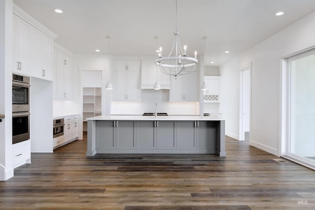 kitchen with a sink, white cabinets, dark wood-type flooring, and a kitchen island with sink