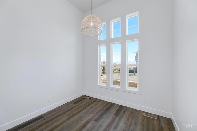 unfurnished room featuring dark wood-style floors, visible vents, baseboards, and a towering ceiling