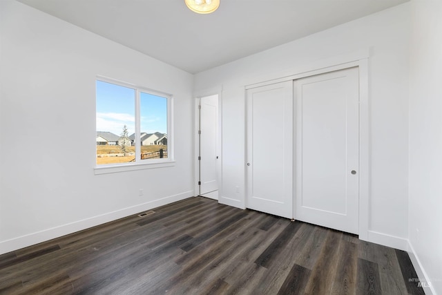 unfurnished bedroom featuring visible vents, baseboards, dark wood-type flooring, and a closet