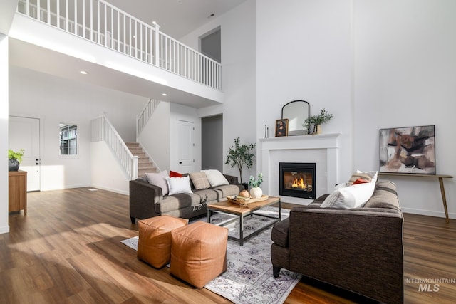 living room featuring a glass covered fireplace, stairway, baseboards, and wood finished floors