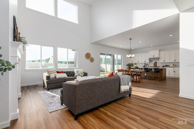 living area featuring wood finished floors, baseboards, a high ceiling, recessed lighting, and a notable chandelier