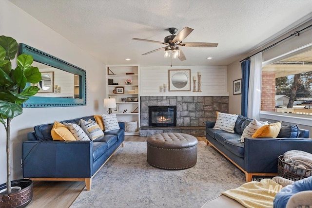 living room with ceiling fan, a textured ceiling, a stone fireplace, and wood finished floors