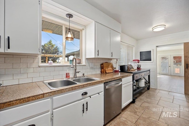 kitchen featuring a sink, white cabinets, stainless steel dishwasher, decorative light fixtures, and tasteful backsplash