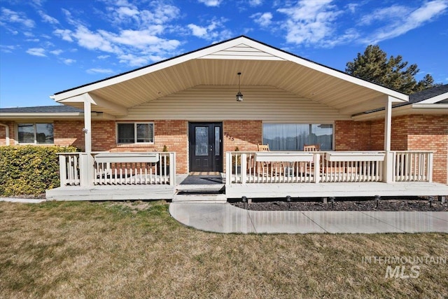 back of property featuring brick siding, a deck, and a lawn