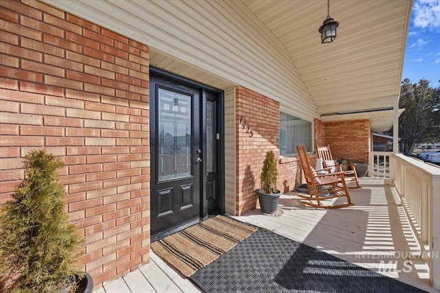 doorway to property with covered porch and brick siding