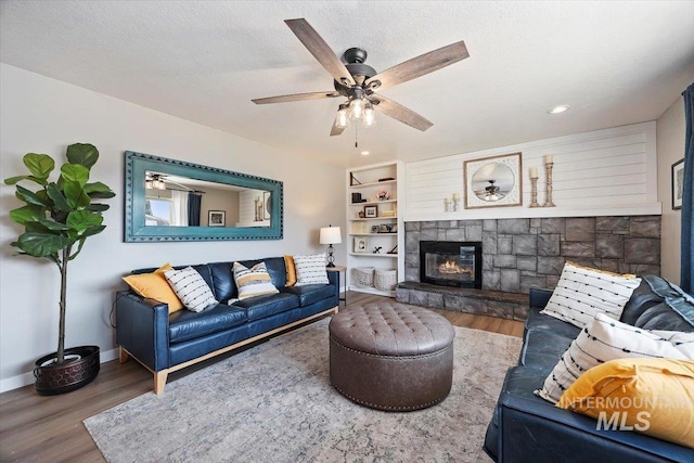 living room featuring a ceiling fan, a textured ceiling, wood finished floors, a fireplace, and baseboards