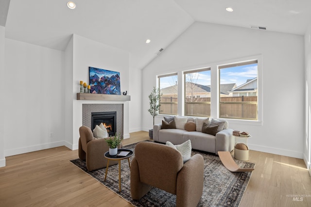 living room with a tiled fireplace, vaulted ceiling, and light hardwood / wood-style flooring