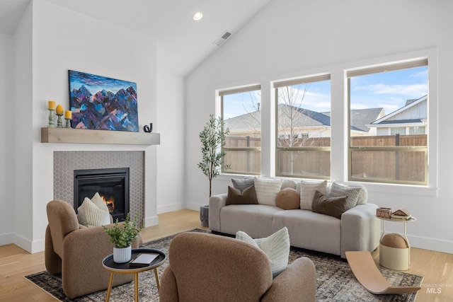 living room featuring lofted ceiling, a tile fireplace, and light wood-type flooring