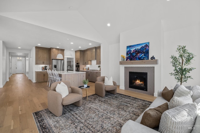 living room with high vaulted ceiling, light wood-type flooring, a tiled fireplace, and sink