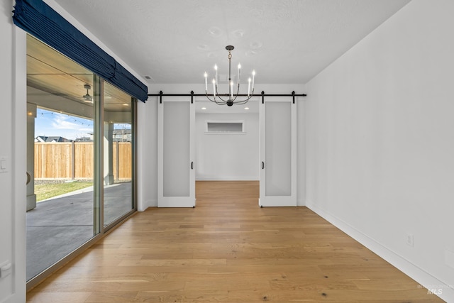 unfurnished dining area featuring a notable chandelier, a barn door, and wood-type flooring