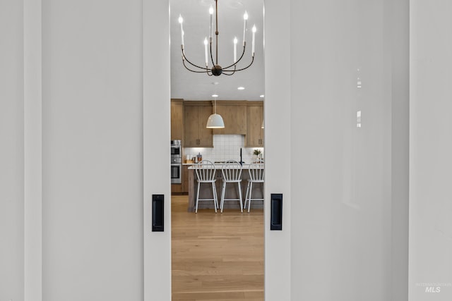 kitchen with wood-type flooring, double oven, a breakfast bar, an inviting chandelier, and tasteful backsplash