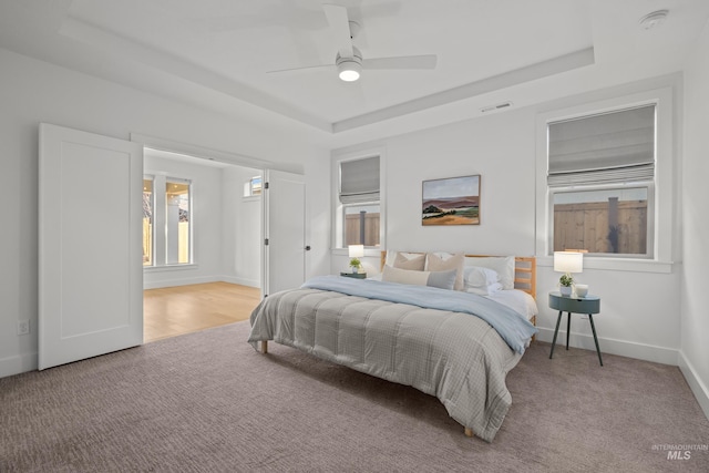 bedroom featuring light colored carpet, ceiling fan, and a tray ceiling