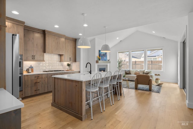 kitchen with light hardwood / wood-style flooring, hanging light fixtures, lofted ceiling, a kitchen island with sink, and appliances with stainless steel finishes