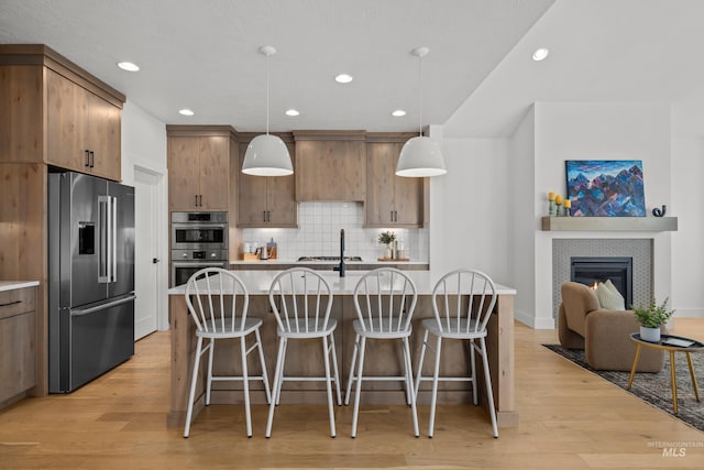 kitchen with a kitchen breakfast bar, a kitchen island with sink, appliances with stainless steel finishes, pendant lighting, and light hardwood / wood-style flooring