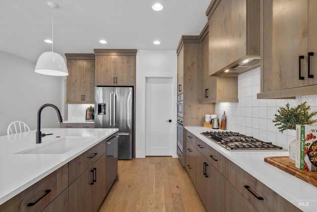 kitchen featuring light hardwood / wood-style flooring, custom exhaust hood, hanging light fixtures, appliances with stainless steel finishes, and sink