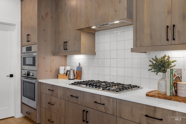 kitchen with stainless steel gas stovetop, light hardwood / wood-style flooring, tasteful backsplash, and premium range hood