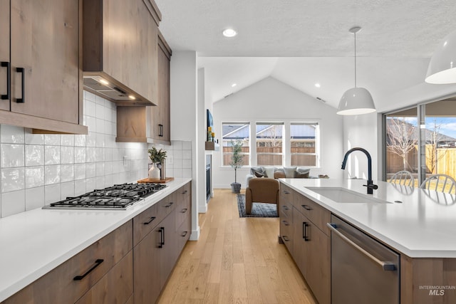 kitchen featuring sink, decorative light fixtures, lofted ceiling, custom range hood, and appliances with stainless steel finishes