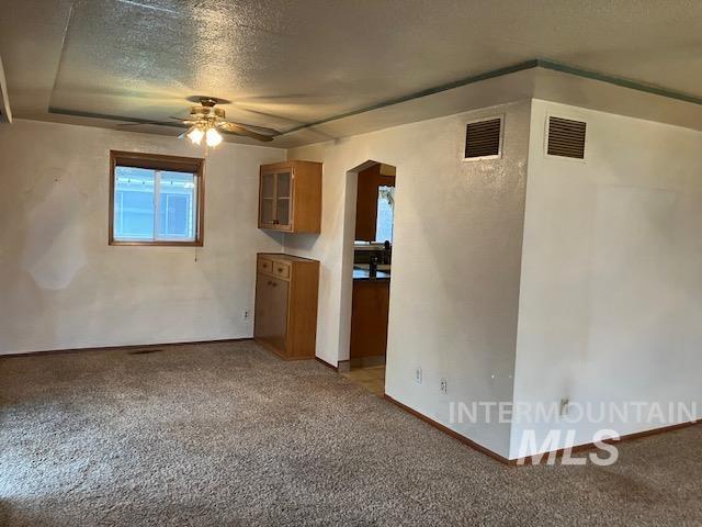 carpeted empty room with ceiling fan and a textured ceiling