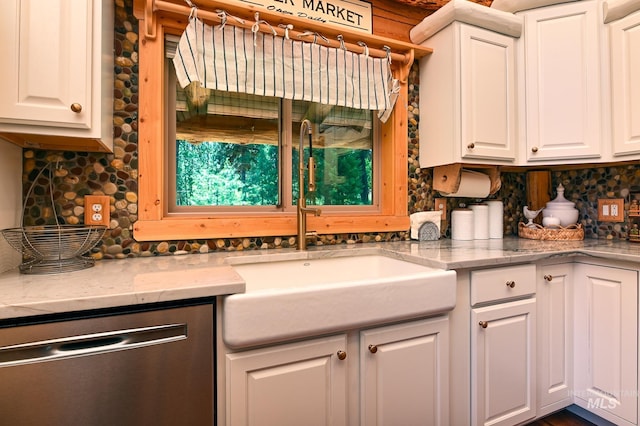 kitchen featuring tasteful backsplash, stainless steel dishwasher, white cabinets, a sink, and light stone countertops